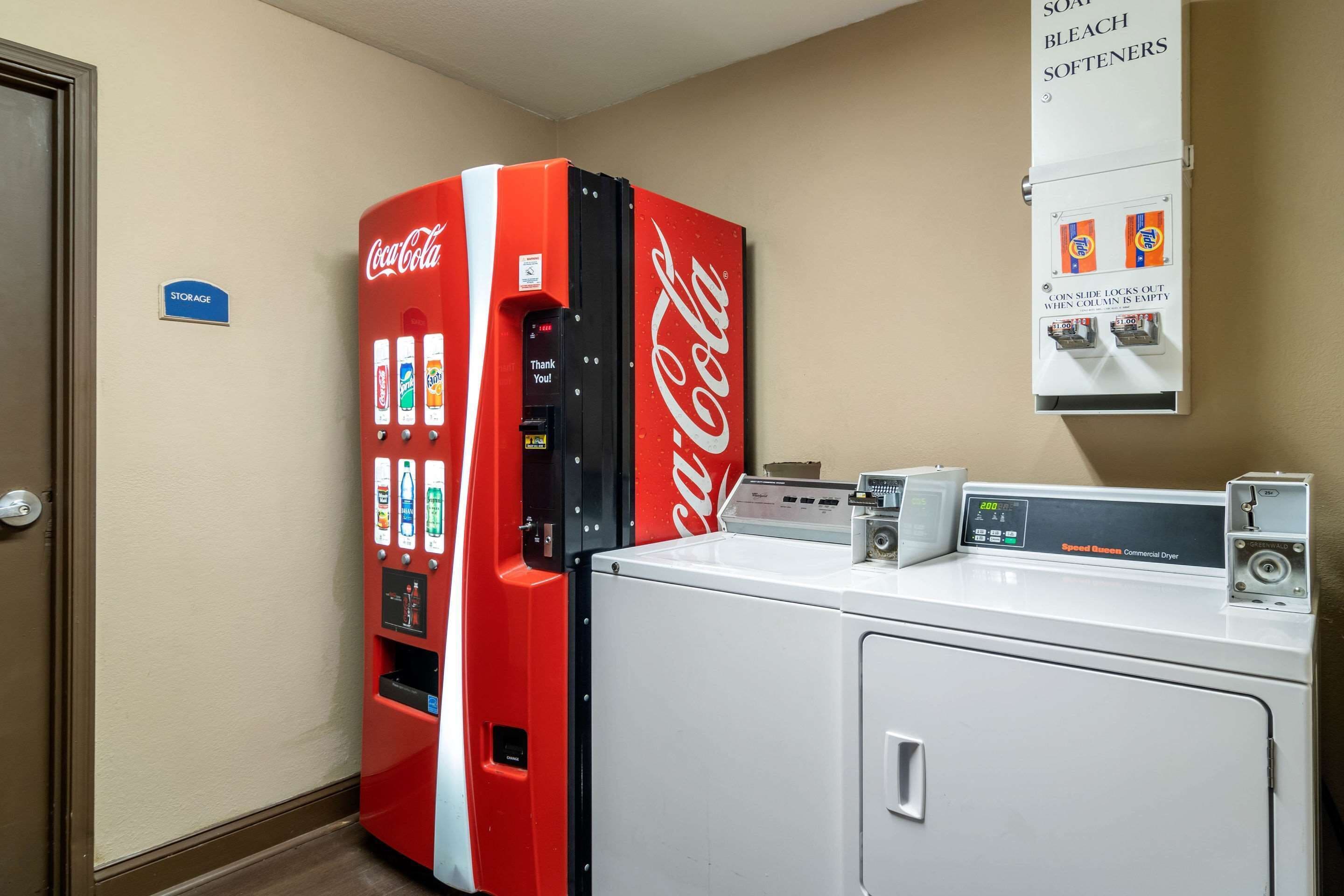 A laundry area with a commercial dryer and a Coca-Cola vending machine.