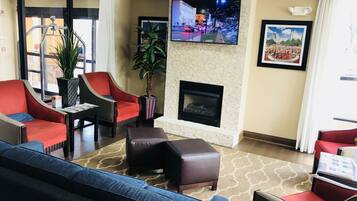 A hotel lobby with a fireplace, seating area, and a television displaying a cityscape.