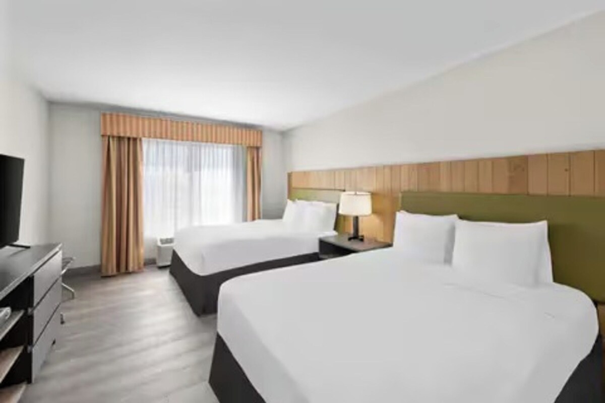 Habitación de hotel con dos camas, televisión, escritorio y ventana con cortinas.