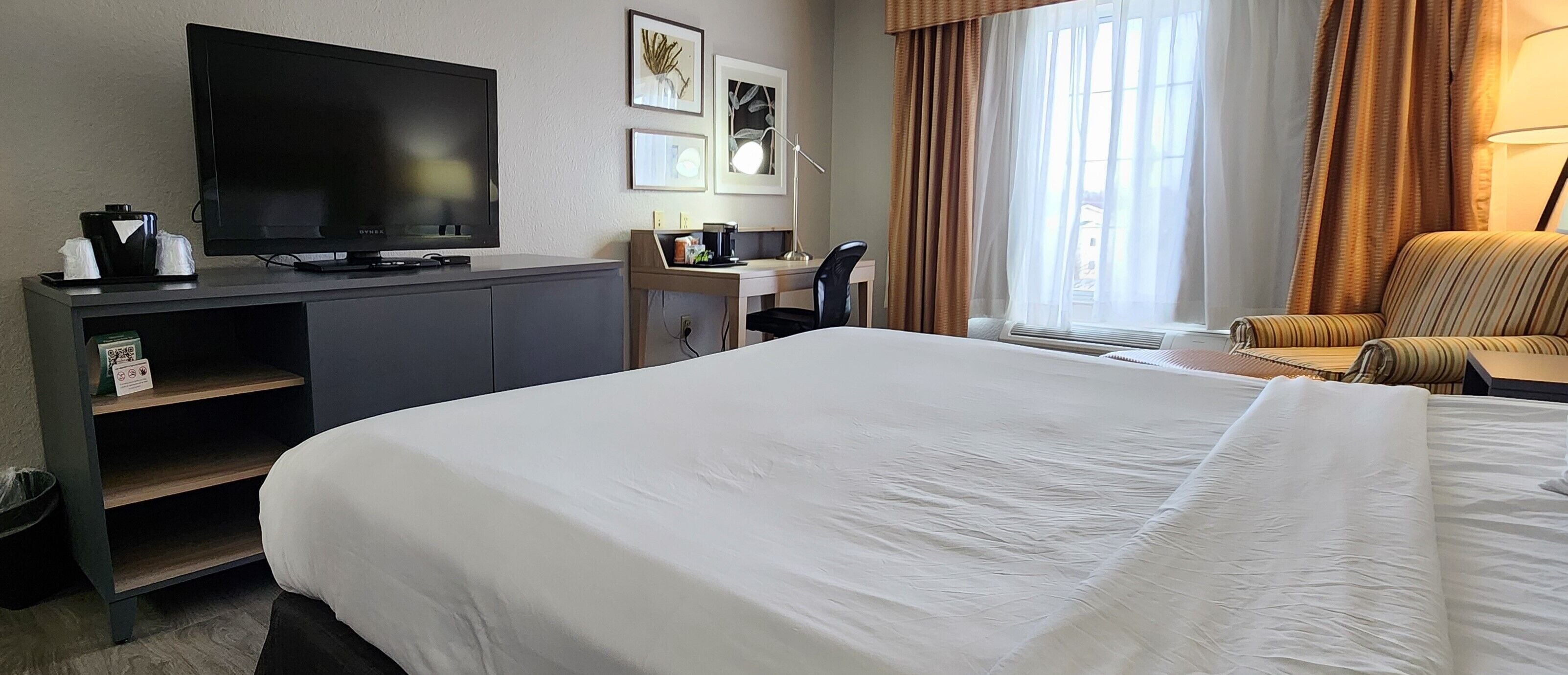 A hotel room with a large bed, a TV, a desk with a chair, and a window with curtains.