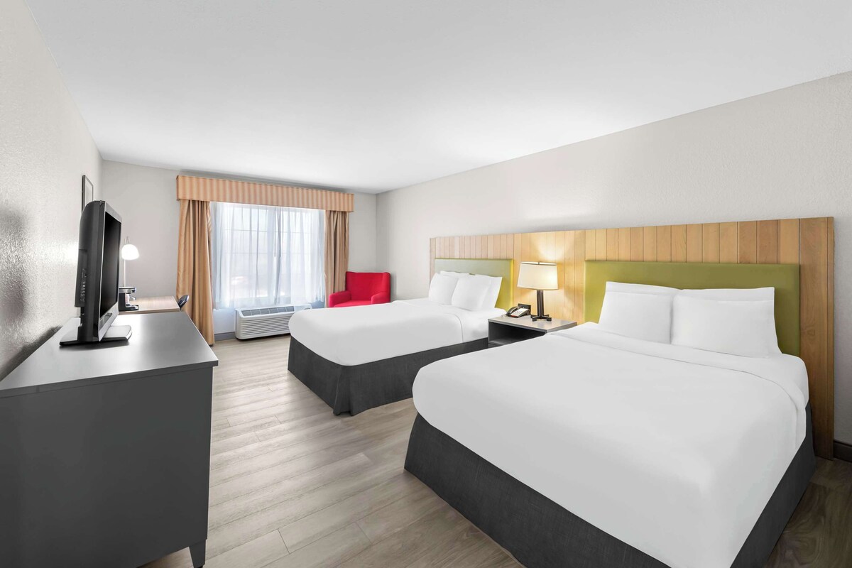 Ein Hotelzimmer mit zwei Betten, einem Schreibtisch, einem Fernseher und einem roten Sessel.