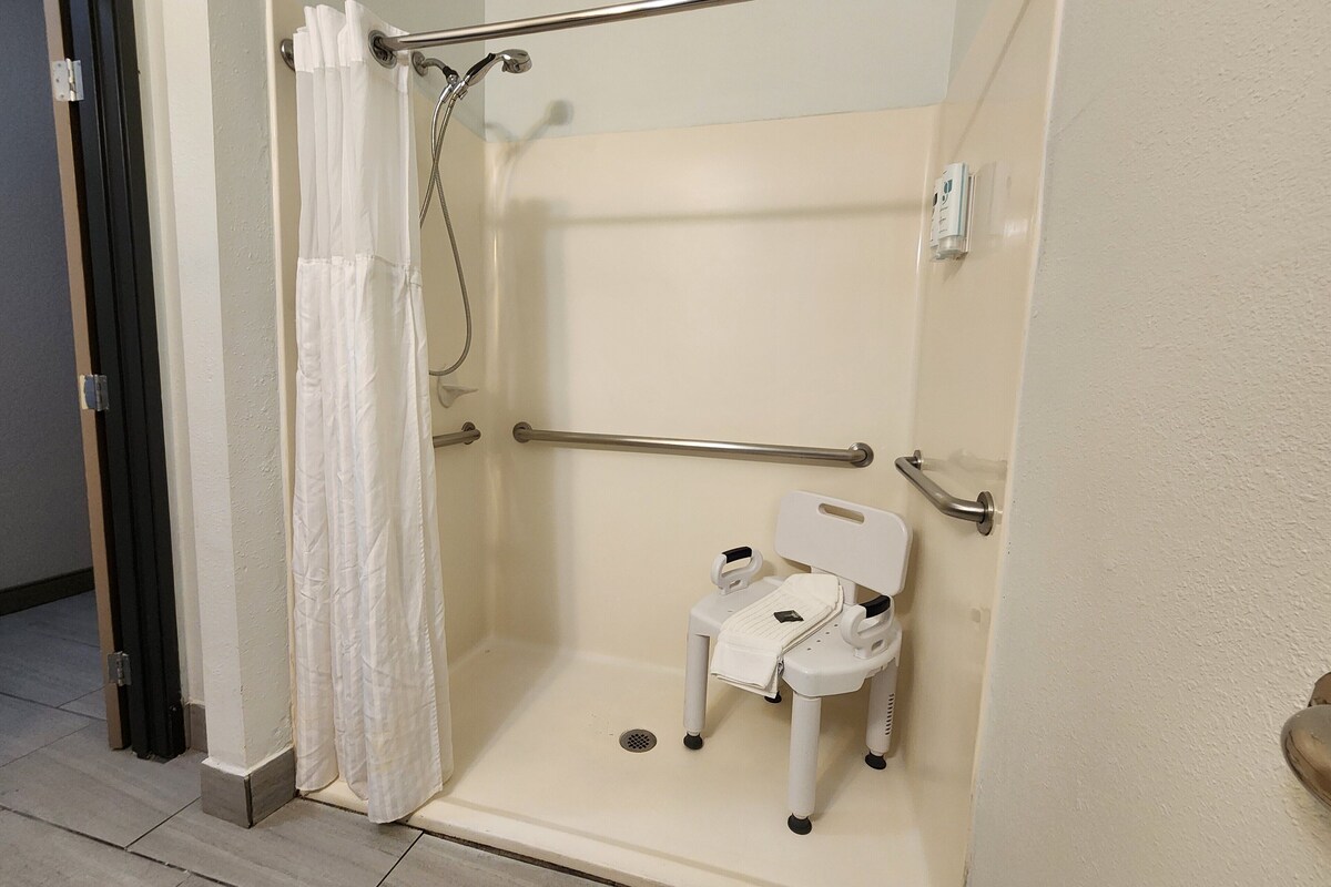 Eine barrierefreie Dusche mit Haltegriff, weißem Duschhocker und Handbrause.
