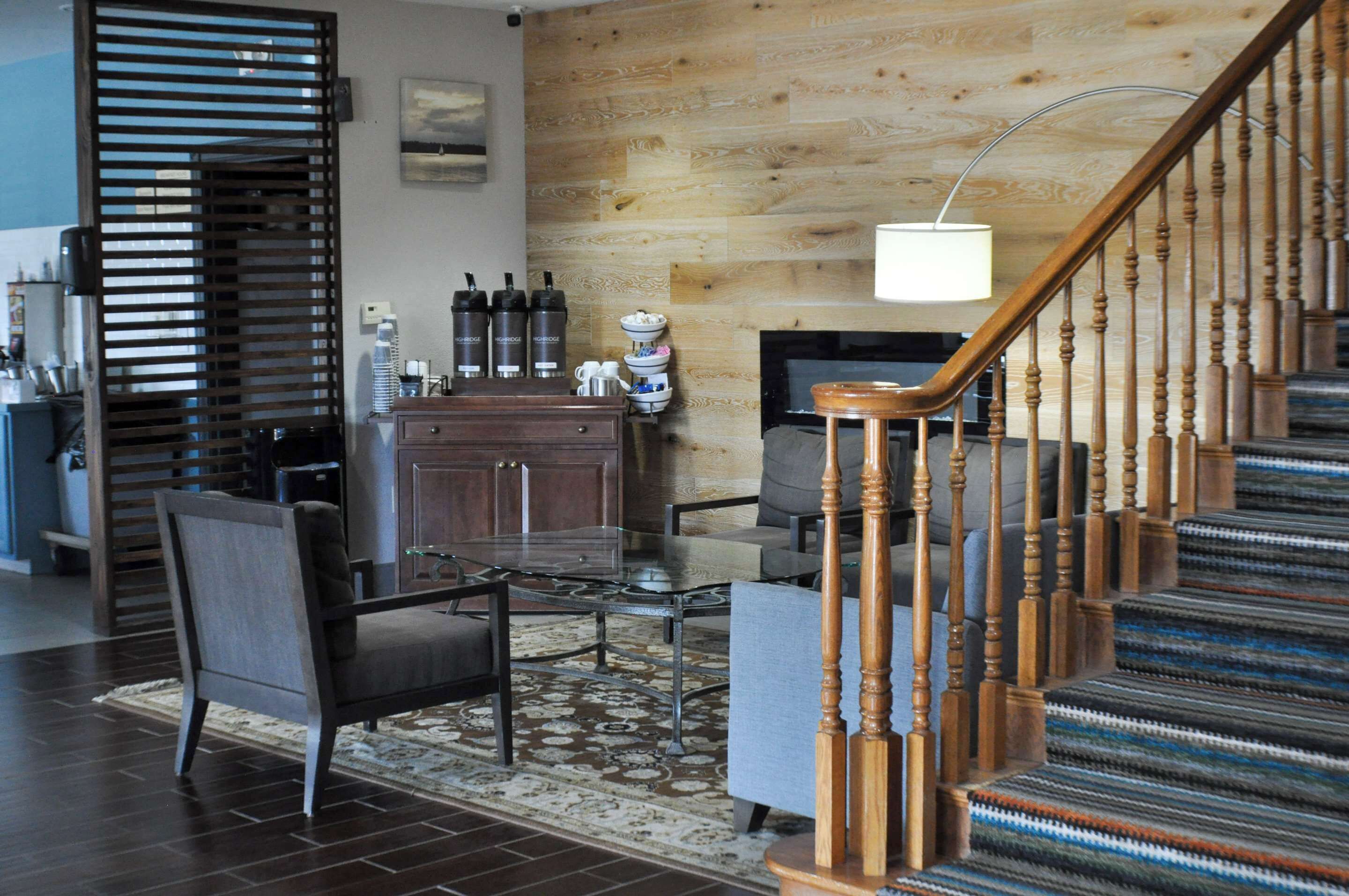 A modern living room with a wooden staircase, a fireplace, and a coffee station.