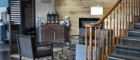 A modern living room with a wooden staircase, a fireplace, and a coffee station.