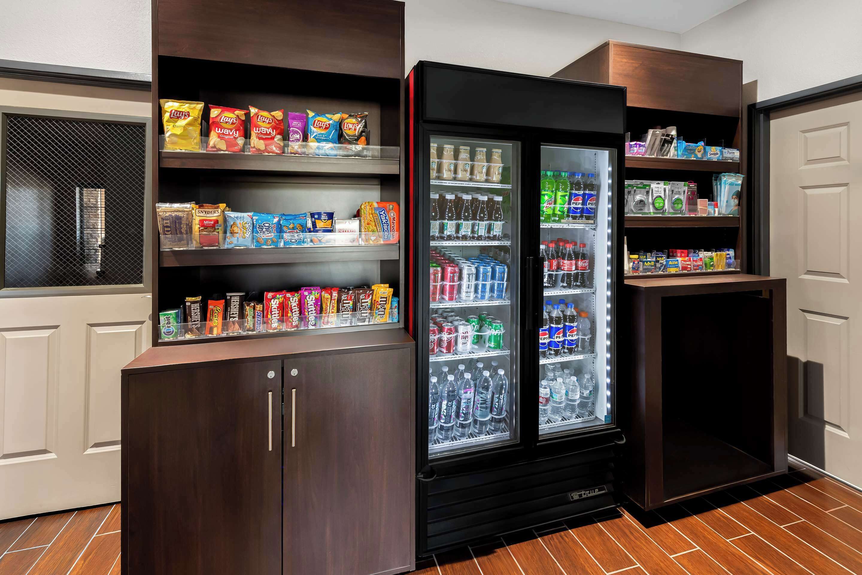 A vending machine with snacks and drinks, a small refrigerator, and a shelf with toiletries.