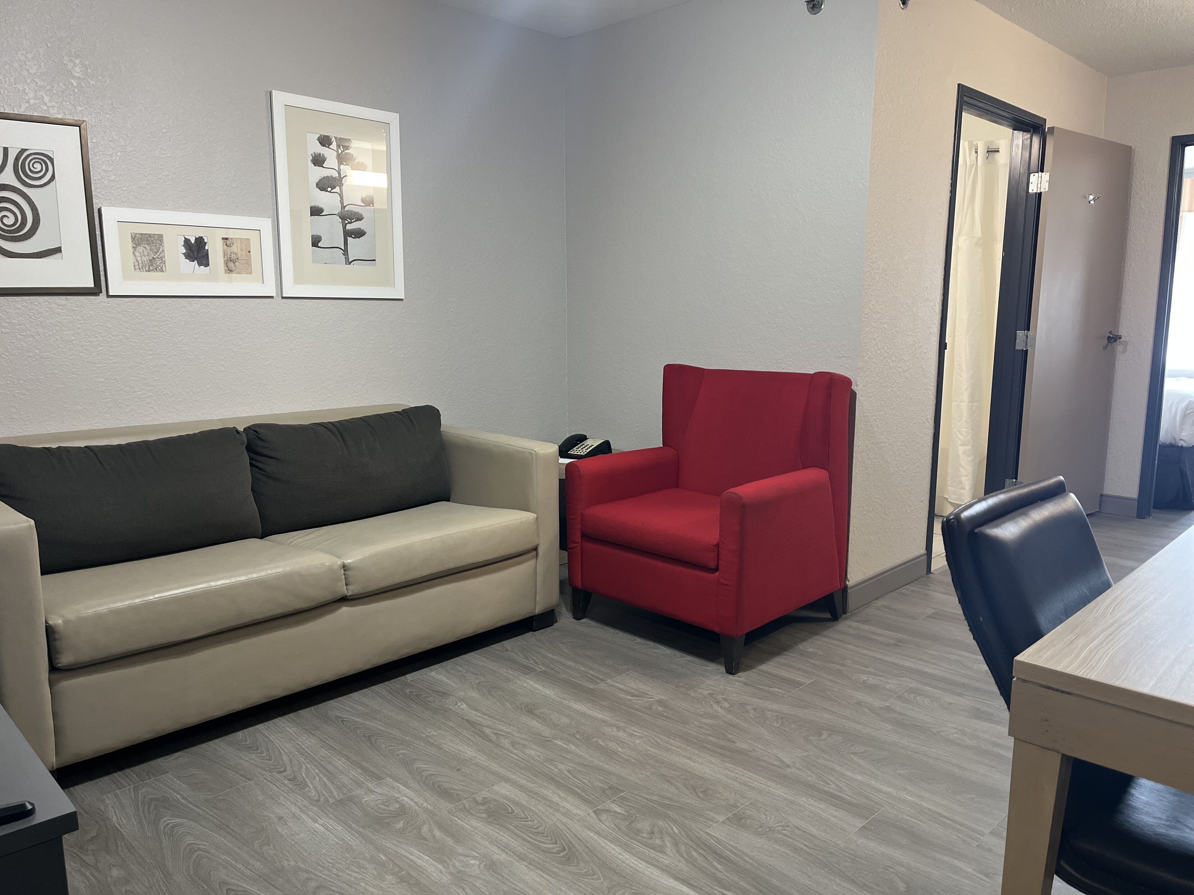 Une pièce avec un canapé beige, un fauteuil rouge, une table à manger en bois et des œuvres d’art encadrées accrochées au mur.