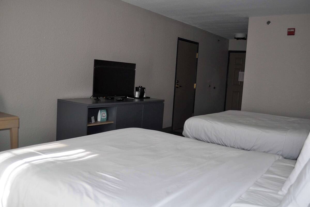 A hotel room with two beds, a television on a dresser, and a door.