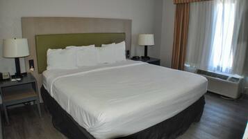 A hotel room with a large bed, two bedside tables with lamps, a window with curtains, and an air conditioning unit.
