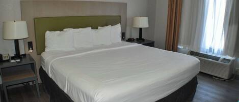 Quarto de hotel com uma cama grande, duas mesas de cabeceira com luminárias, uma janela com cortinas e um ar condicionado.