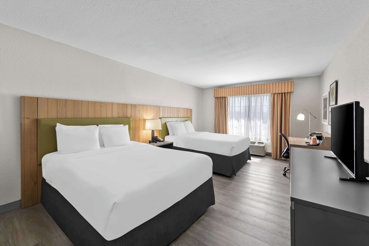 Ein Hotelzimmer mit zwei Betten, einem Schreibtisch, einem Fernseher und einem fenster mit Vorhängen.