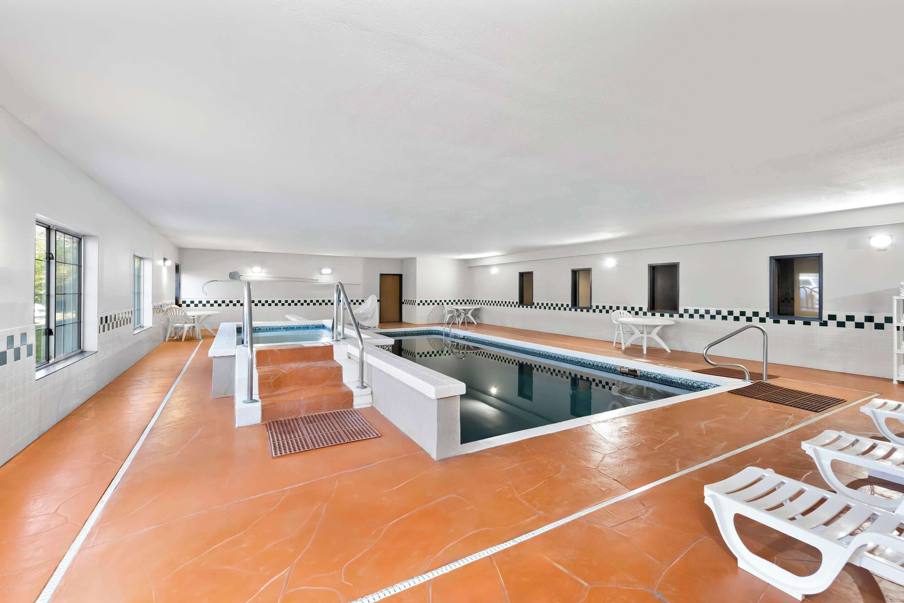 Een modern binnenzwembad met een helder watergedeelte, treden die naar het zwembad leiden en witte lounge fauteuils rondom de rand.