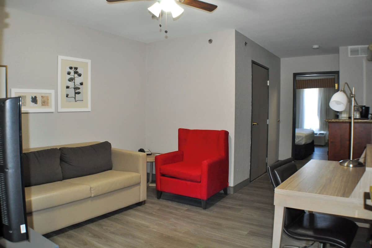A living room with a sofa, a red armchair, a TV, and framed pictures on the wall.