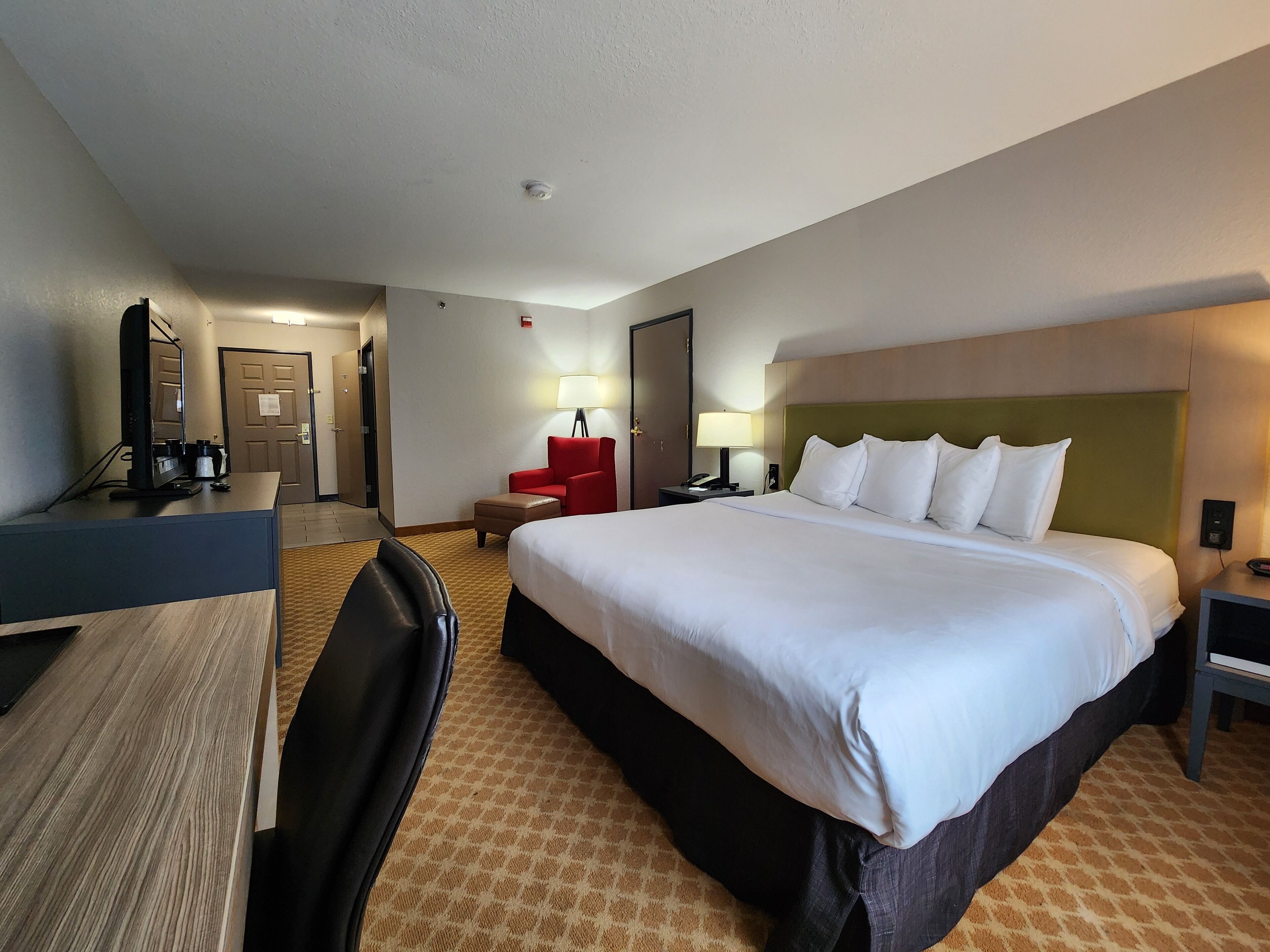 A hotel room with a large bed, a desk, a chair, a lamp, and a television.