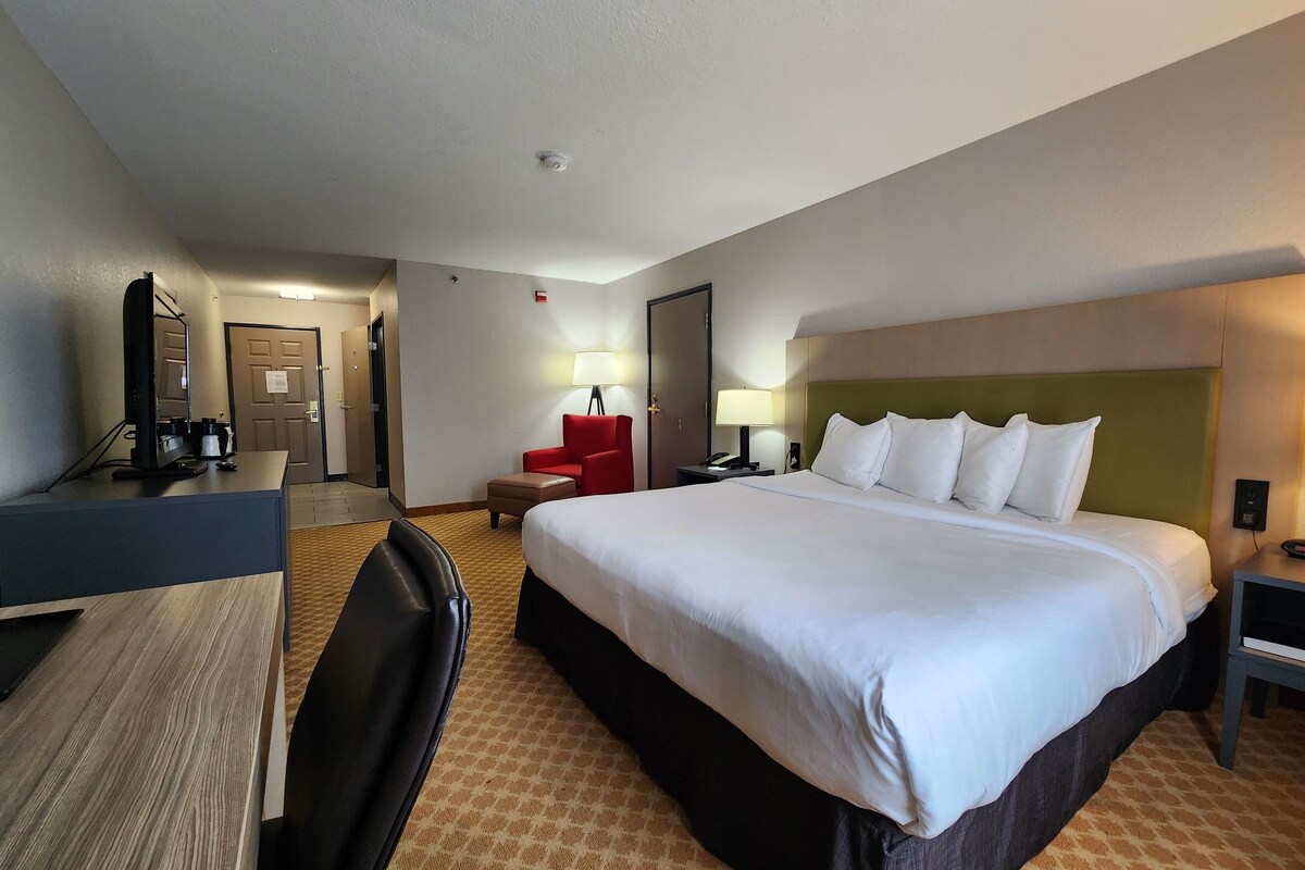 Ein Hotelzimmer mit einem großen Bett, einem Schreibtisch, einem Sessel, einer Lampe und einem Fernseher.
