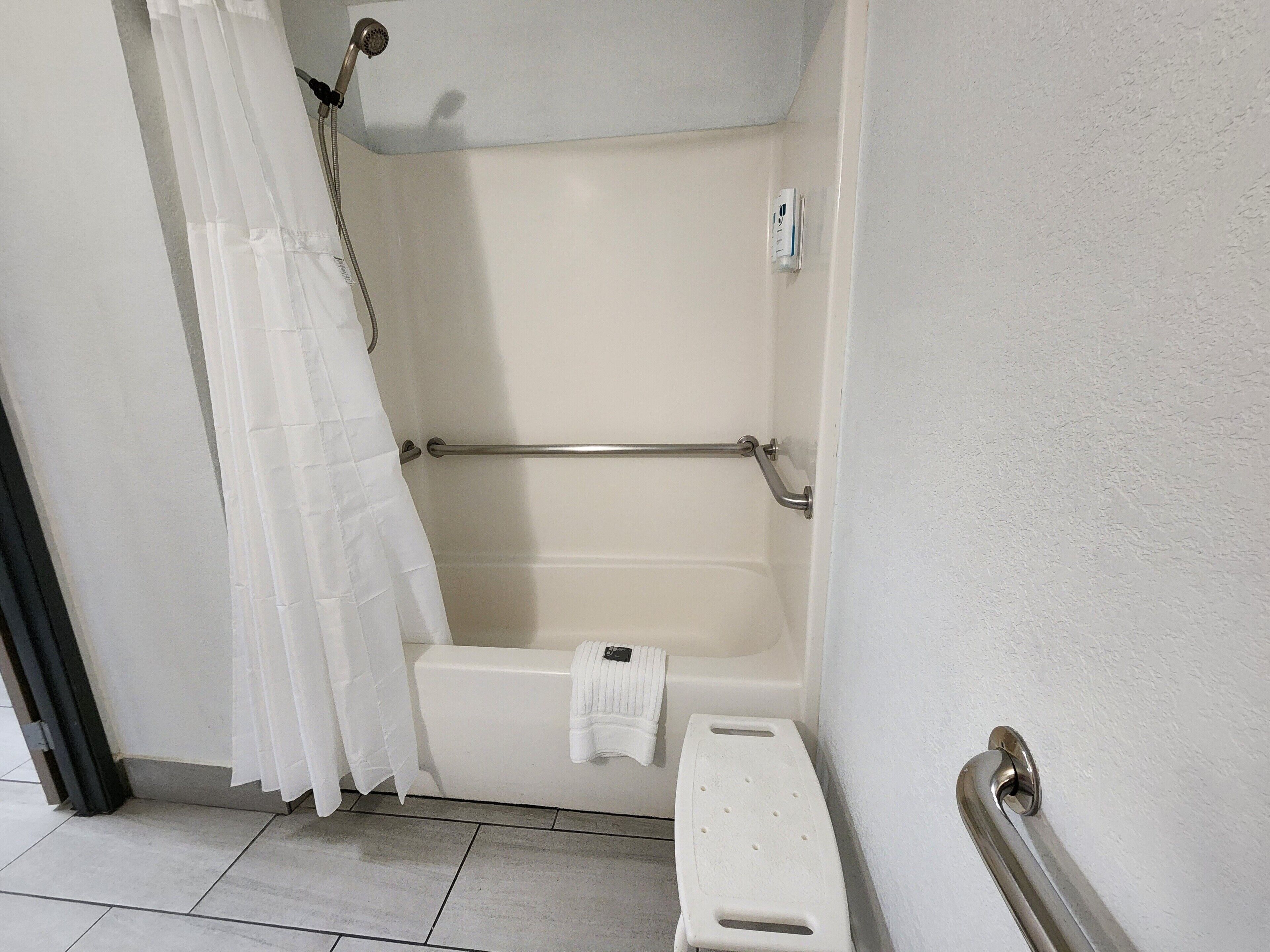 A bathroom with a shower, a grab bar, and a white towel rack.