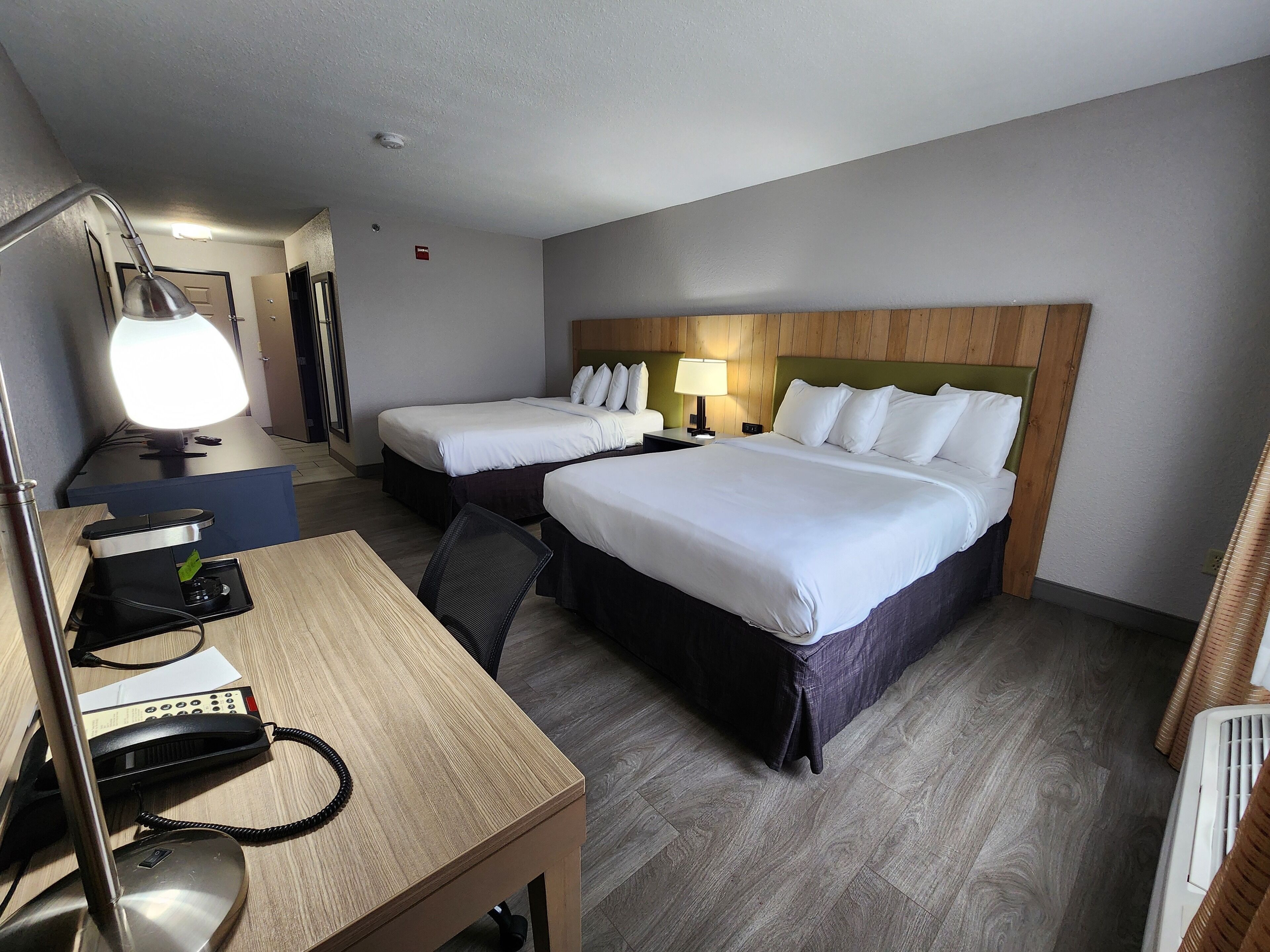 A hotel room with two beds, a desk with a telephone, a lamp, and a chair.