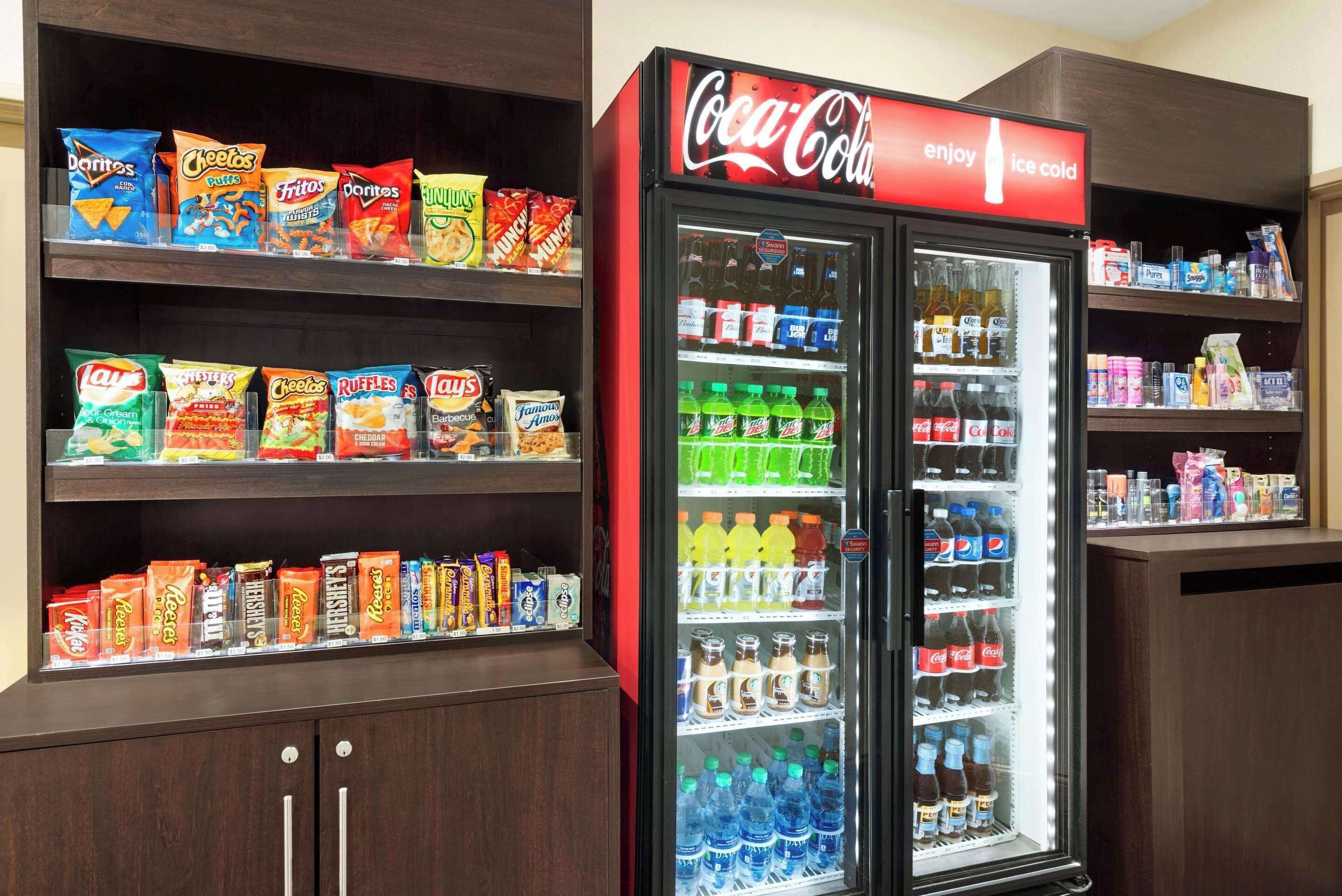Una máquina expendedora llena de bocadillos y un refrigerador Coca-Cola con diversas bebidas.