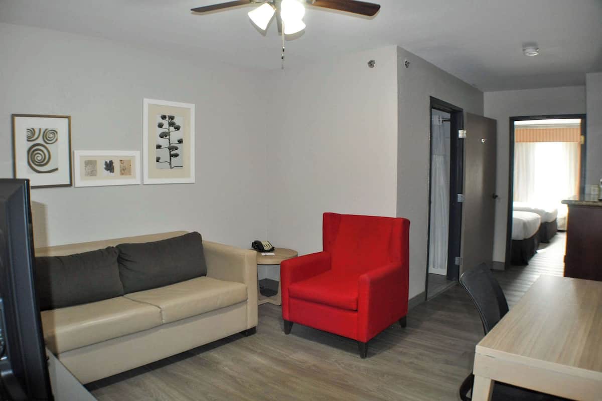 A living room with a beige sofa, a red armchair, a ceiling fan, and framed artwork on the wall.
