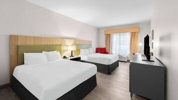 Quarto de hotel com duas camas, uma escrivaninha, uma cadeira, televisão e janela com cortinas.