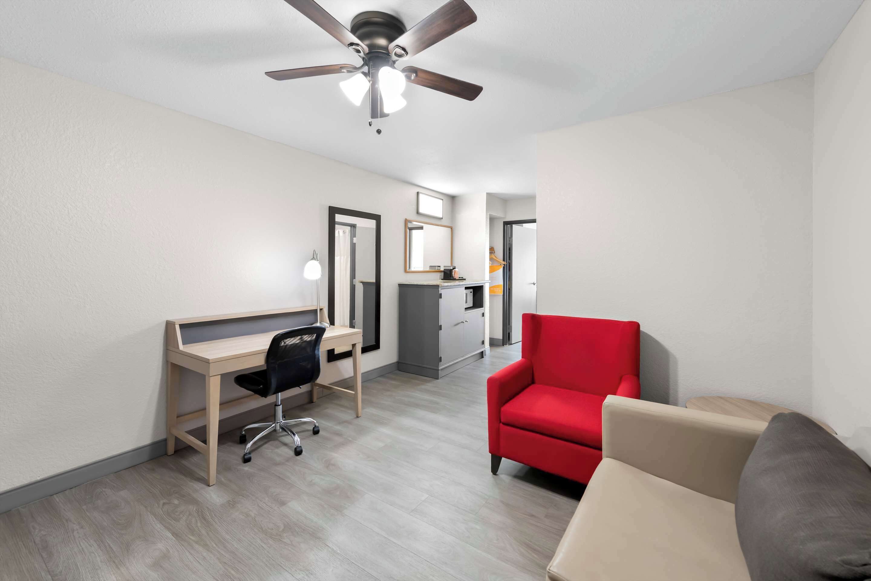 Une chambre moderne avec un bureau, une chaise rouge, un canapé beige et un ventilateur de plafond.