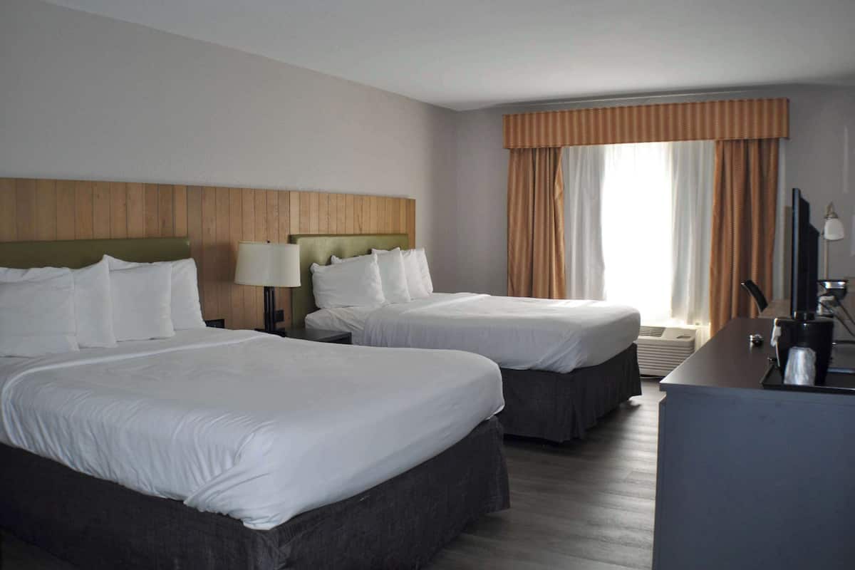 A hotel room with two beds, a desk, a lamp, and a large window with curtains.
