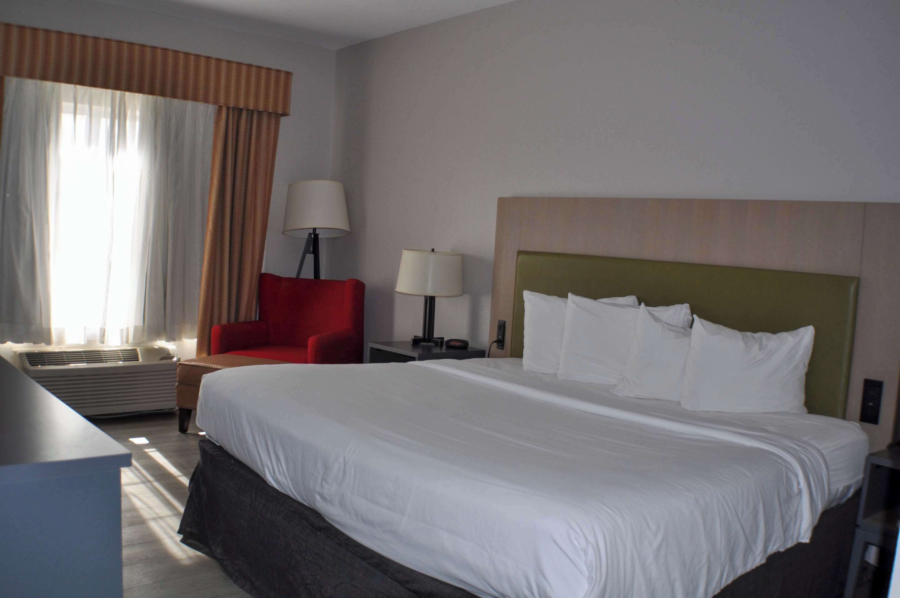Una camera d'albergo con un letto grande, una poltrona rossa, due lampade ai piedi del letto e una finestra con tende.