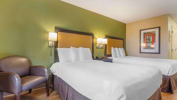 A hotel room with two beds, a chair, and a nightstand with lamps.