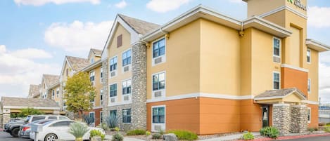 A multi-story hotel with a yellow facade, stone accents, and a parking lot with several cars.