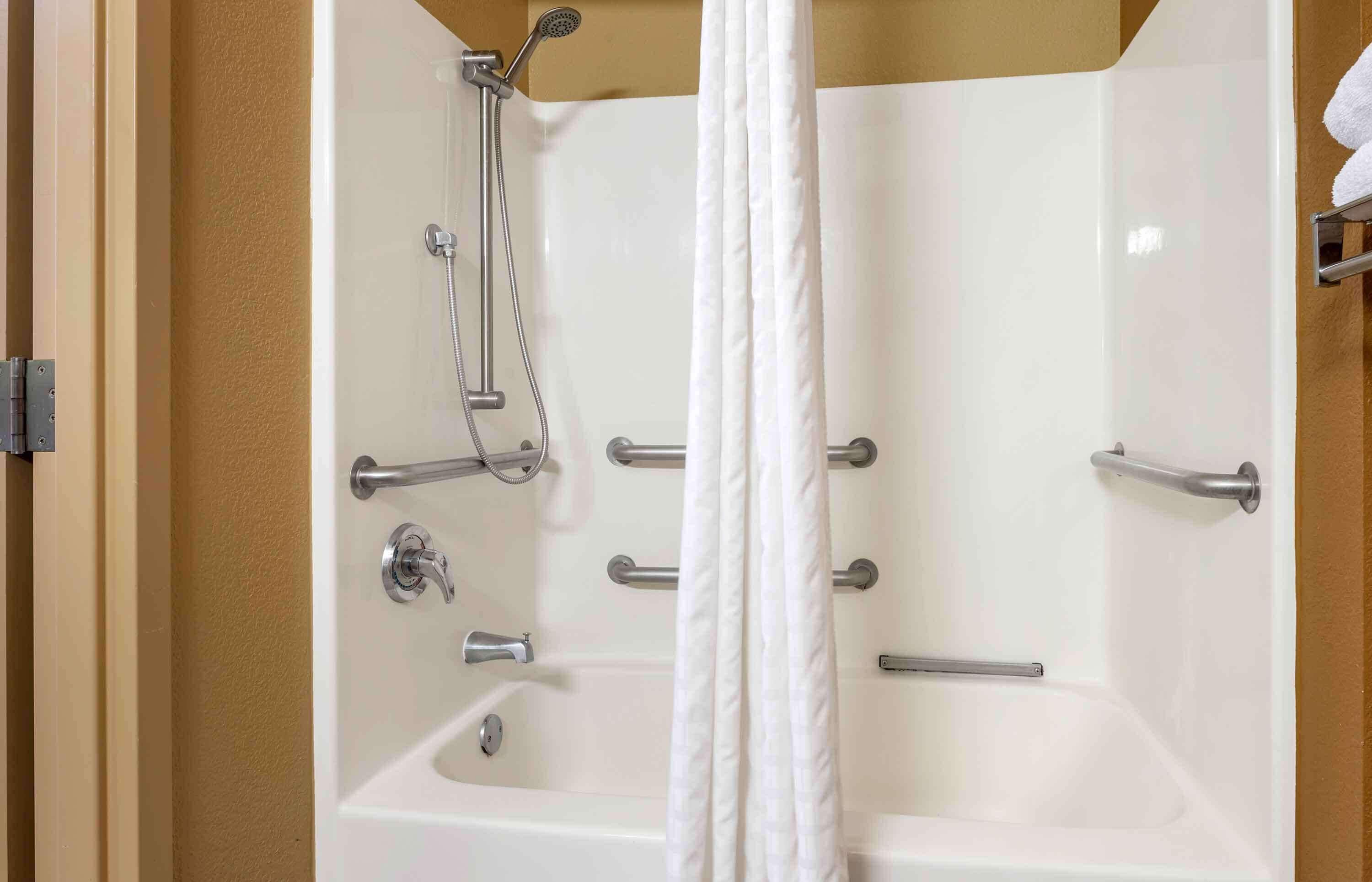 A modern bathroom with a bathtub, shower, and handrails.