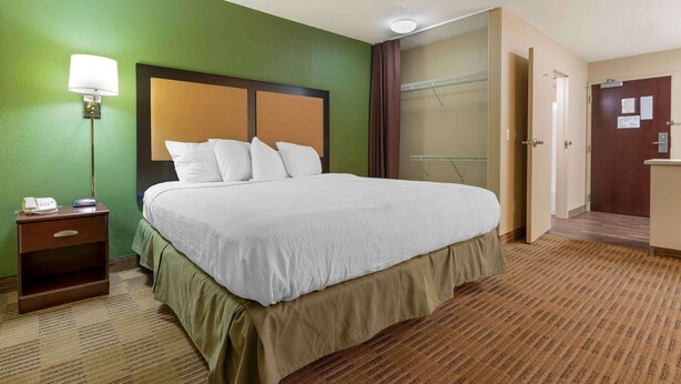 Une chambre d’hôtel avec un grand lit, une table de chevet avec une lampe, une armoire et une porte.