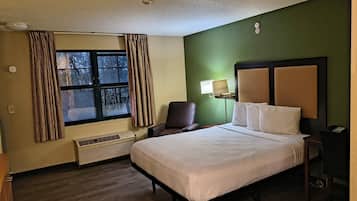 A hotel room with a bed, a chair, a desk, a lamp, and a window with curtains.