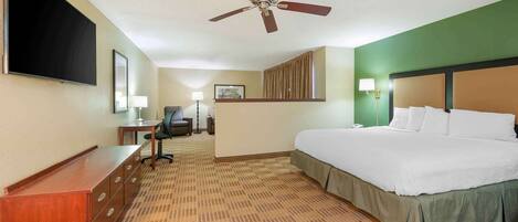 A hotel room with a bed, desk, chair, flat-screen TV, ceiling fan, and a large window.
