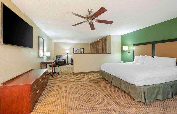 Habitación de hotel con cama, escritorio, silla, televisión de pantalla plana, ventilador de techo y un ventanal grande.