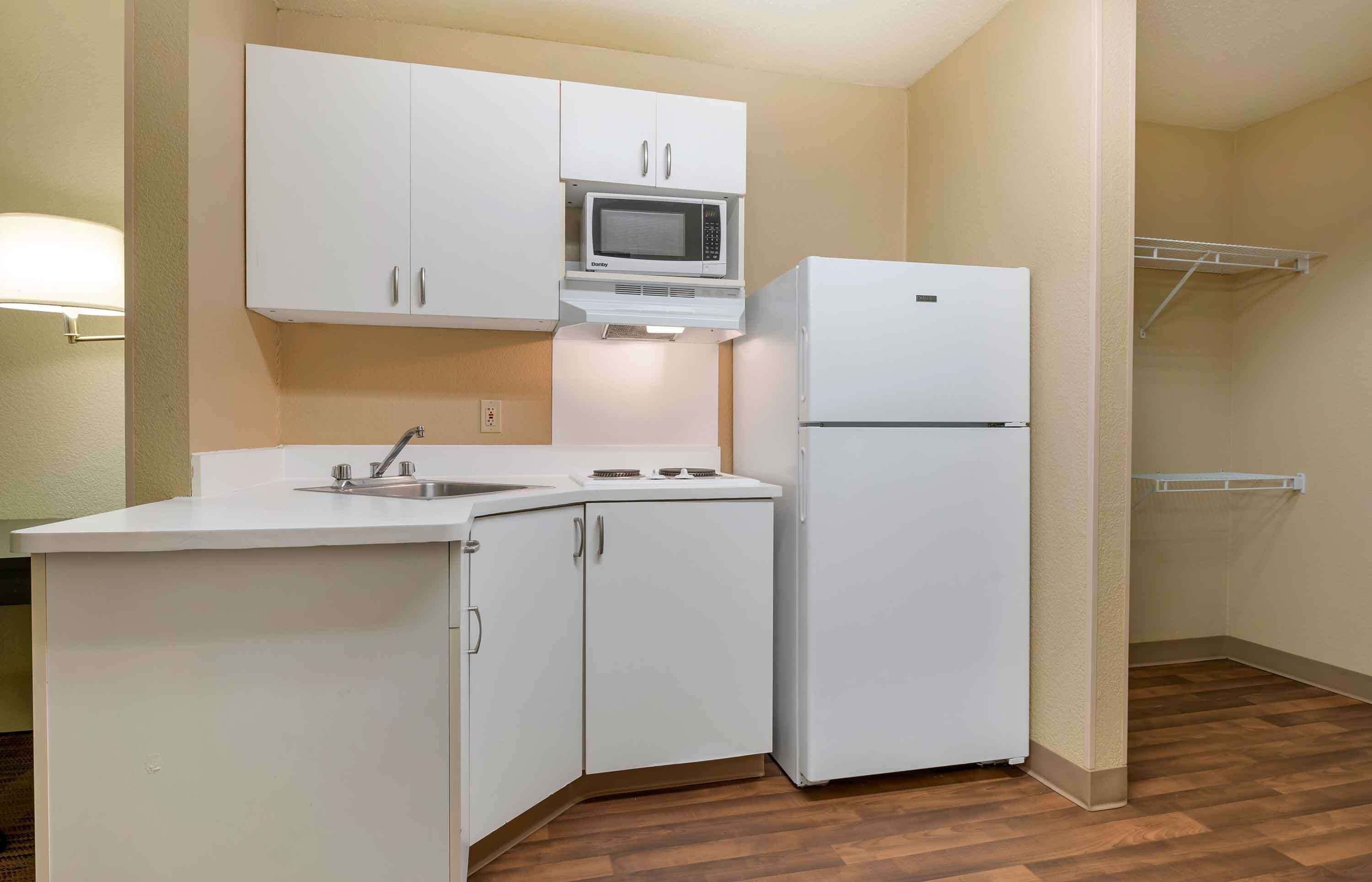 A compact kitchen with white cabinets, a microwave, a refrigerator, and a sink.