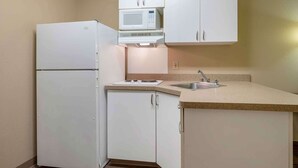 Une cuisine compacte avec des meubles blancs, un four à micro-ondes encastré, un réfrigérateur et un évier.