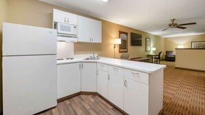 Une cuisine compacte avec des meubles blancs, un four à micro-ondes et un réfrigérateur. On y trouve un coin repas avec une table et des chaises, ainsi qu'un ventilateur de plafond.