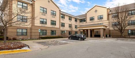 A multi-story building with a parking lot, a car, and a tree.