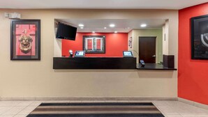 A reception desk with a red wall, a framed picture, and a flat-screen TV. - Extended Stay America Select Suites - Austin - Northwest - Lakeline Mall (Austin)