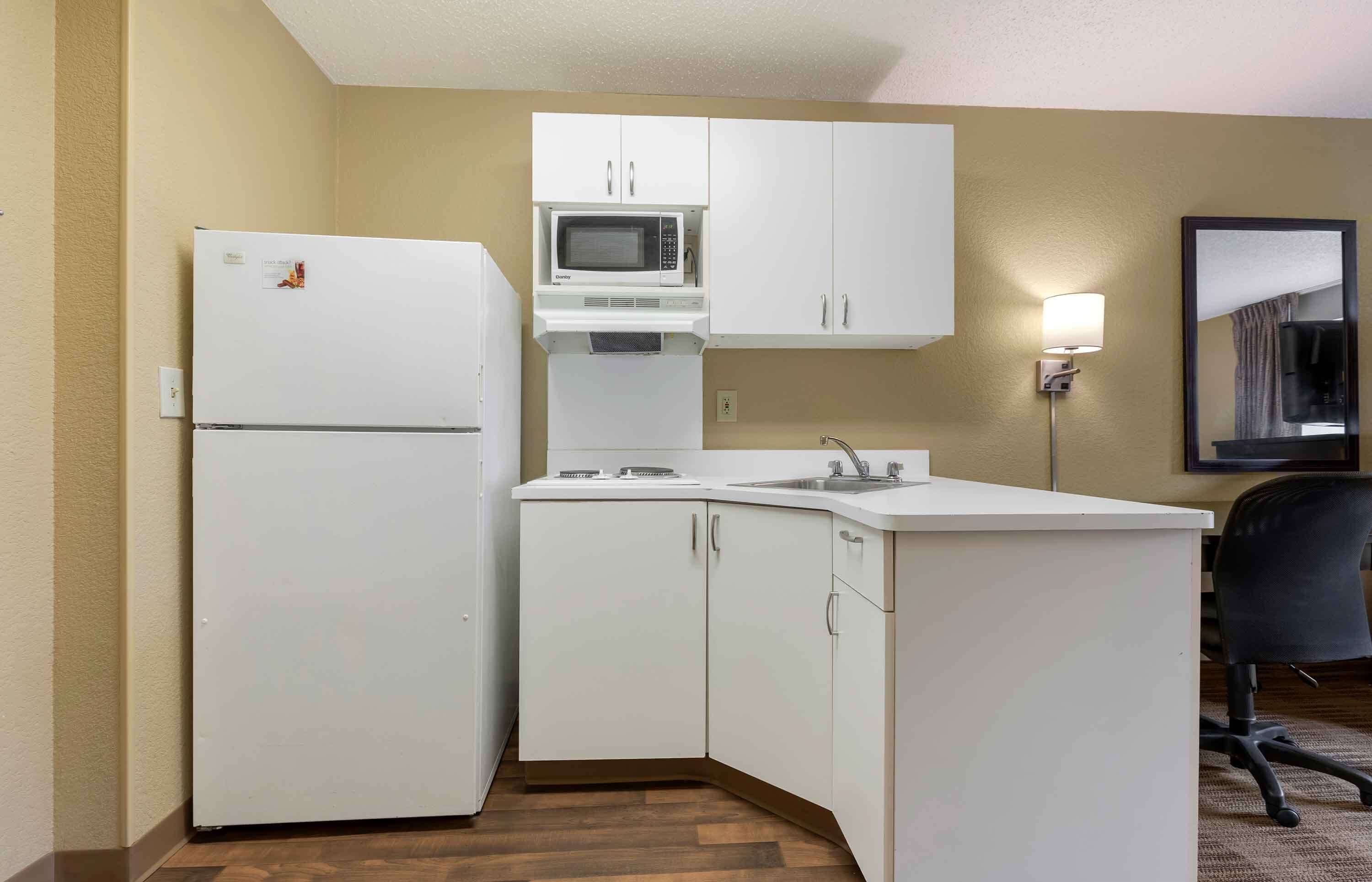 A compact kitchen with white cabinets, a microwave, a refrigerator, and a sink.