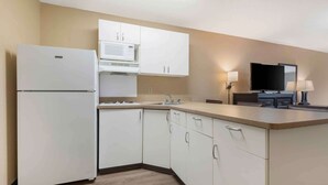 A compact kitchen with white cabinets, a microwave, a refrigerator, a sink, and a flat-screen TV. - Extended Stay America Select Suites - Austin - Northwest - Lakeline Mall (Austin)