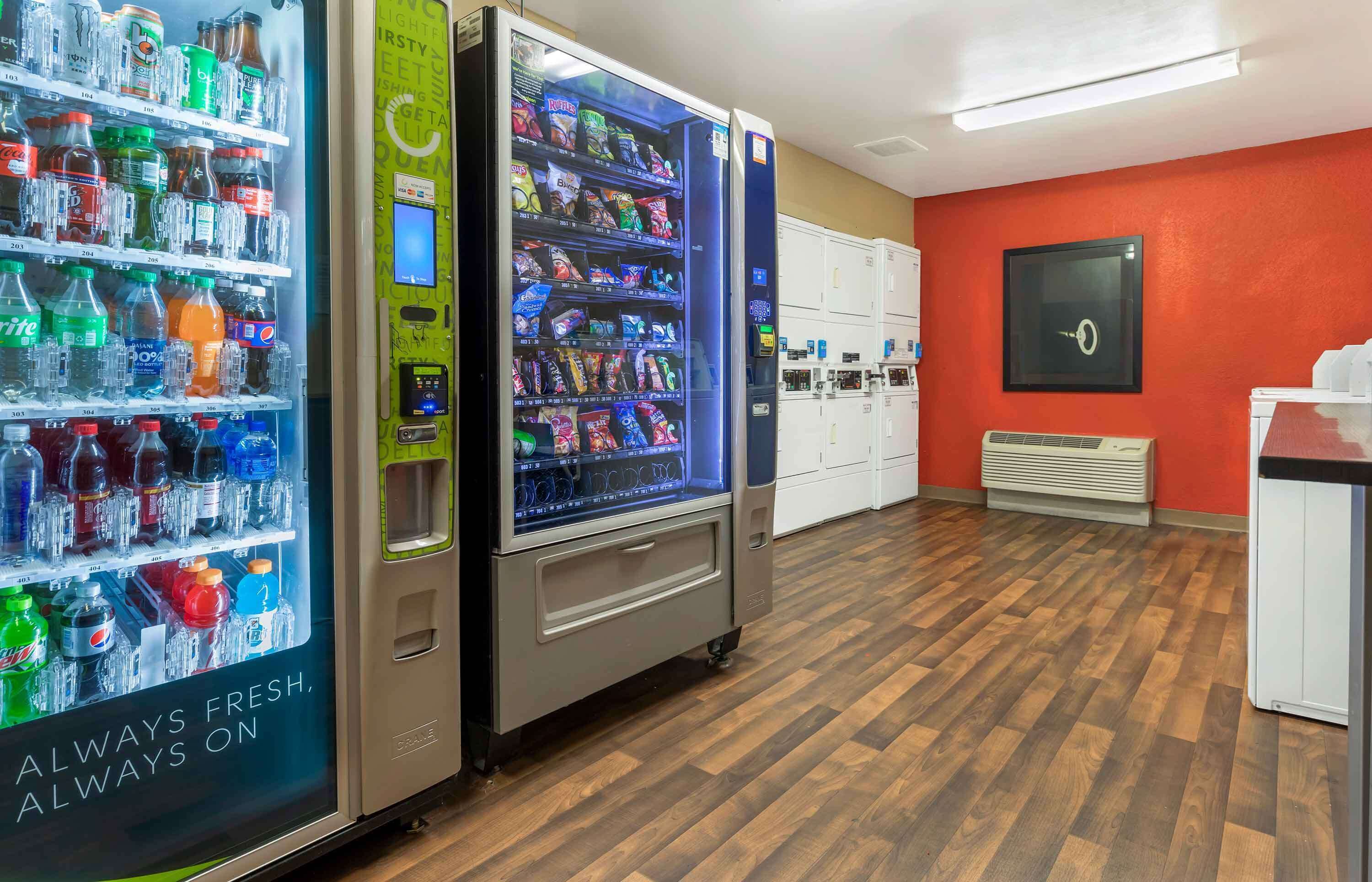 A hotel lobby with a vending machine stocked with beverages and snacks, a white reception desk, and a red accent wall.