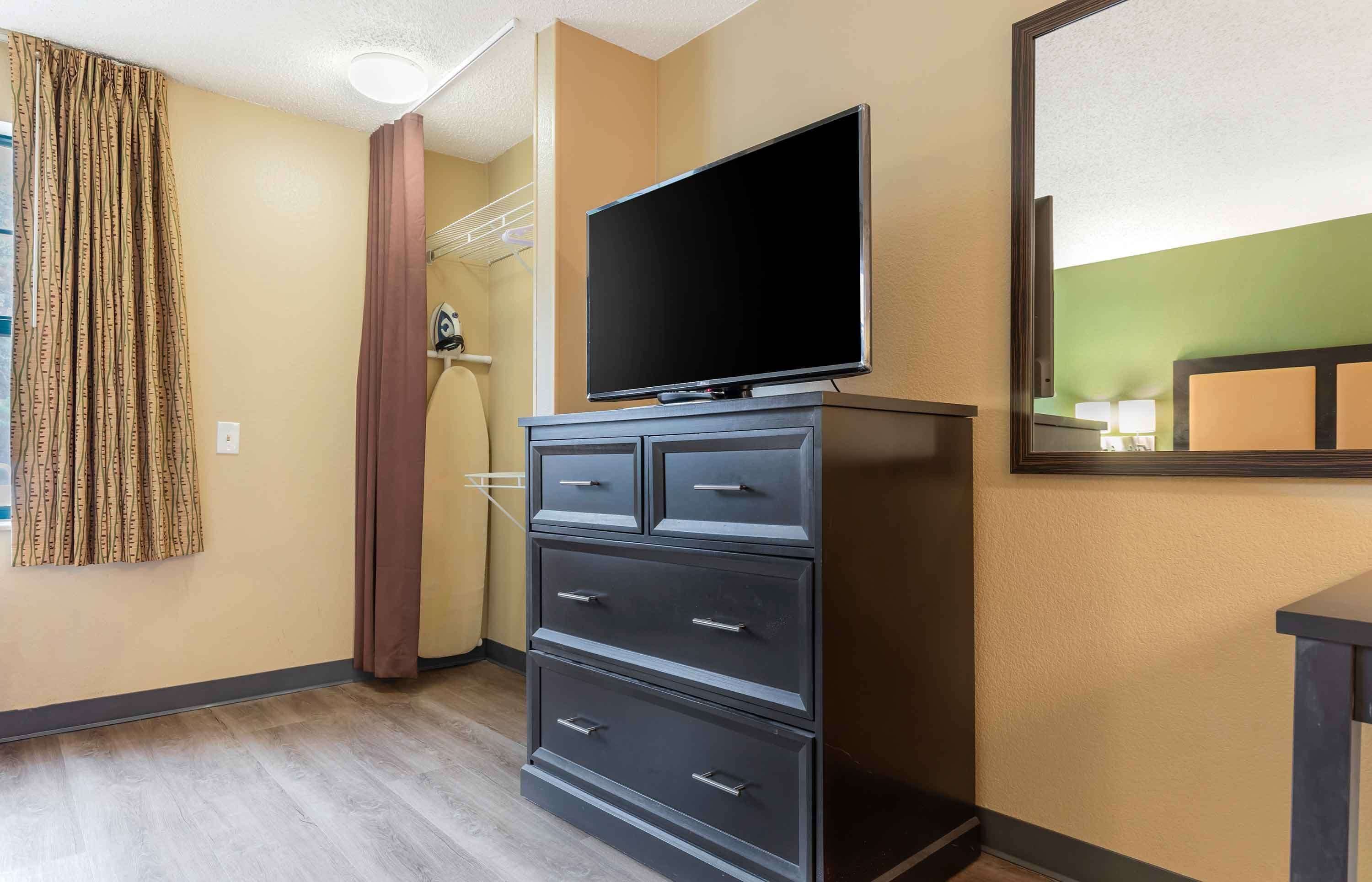 A hotel room with a flat-screen TV on a dresser, a mirror on the wall, and a wooden floor.