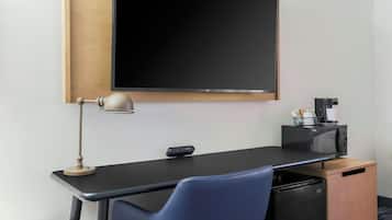 Una habitación de hotel moderna con una televisión de pantalla plana montada en la pared, un escritorio con lámpara, microondas y un refrigerador pequeño.