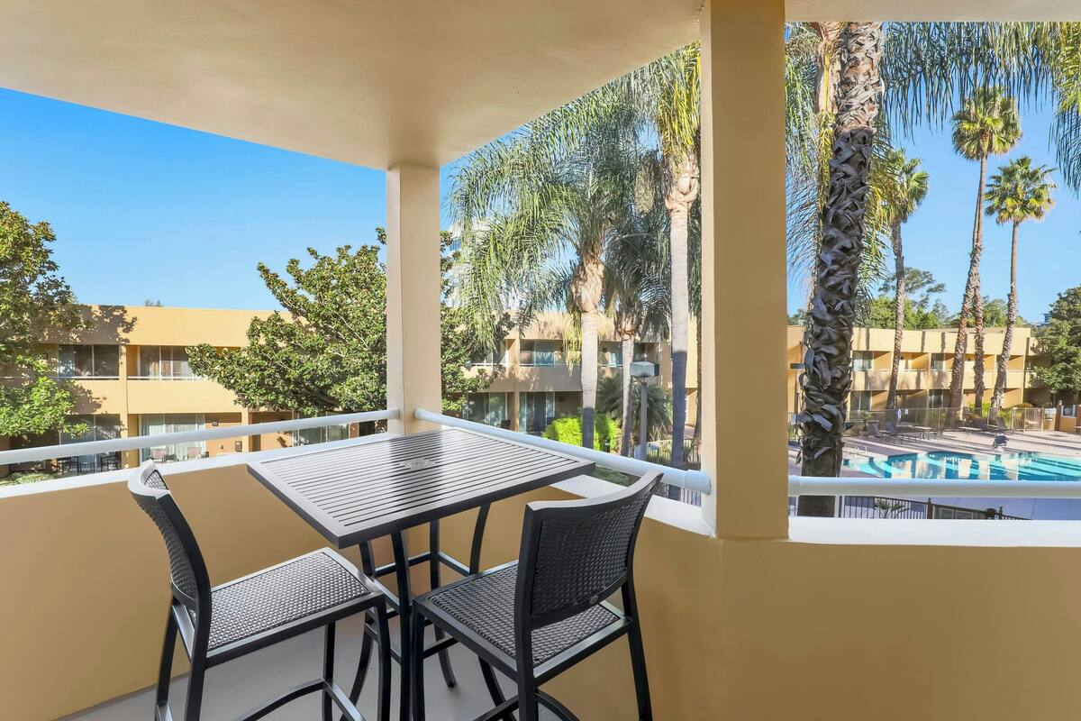 Een balkon met een tafel en stoelen, met uitzicht op een zwembad en palmbomen.