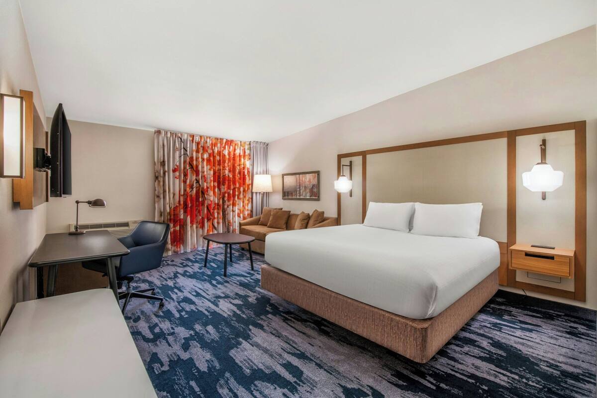 Ein Hotelzimmer mit einem großen Bett, einem Schreibtisch, einem Sessel, einem kleinen Tisch und einer Couch.