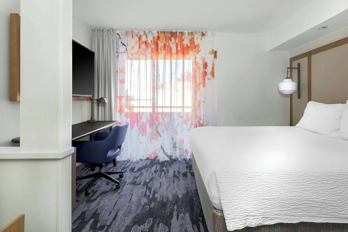 Ein Hotelzimmer mit Bett, Schreibtisch, Stuhl und einem Vorhangfenster.