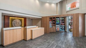 Un espace d’accueil comprenant un comptoir de réception en bois, un élément décoratif mural et un distributeur automatique.