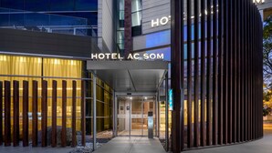 A modern hotel entrance with a glass facade, a visible reception desk, and a sign reading "HOTEL AC SOM." - AC Hotel Som by Marriott (L'Hospitalet de Llobregat)