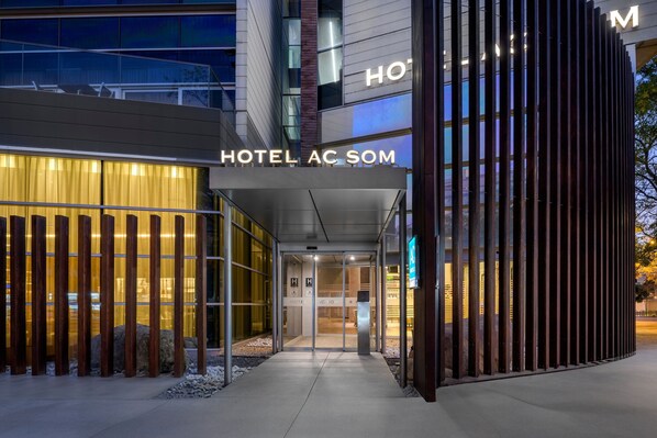 A modern hotel entrance with a glass facade, a visible reception desk, and a sign reading "HOTEL AC SOM." - AC Hotel Som by Marriott (L'Hospitalet de Llobregat)