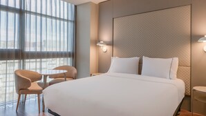 A hotel room with a large bed, two chairs, a small table, and a large window with sheer curtains. - AC Hotel Som by Marriott (L'Hospitalet de Llobregat)
